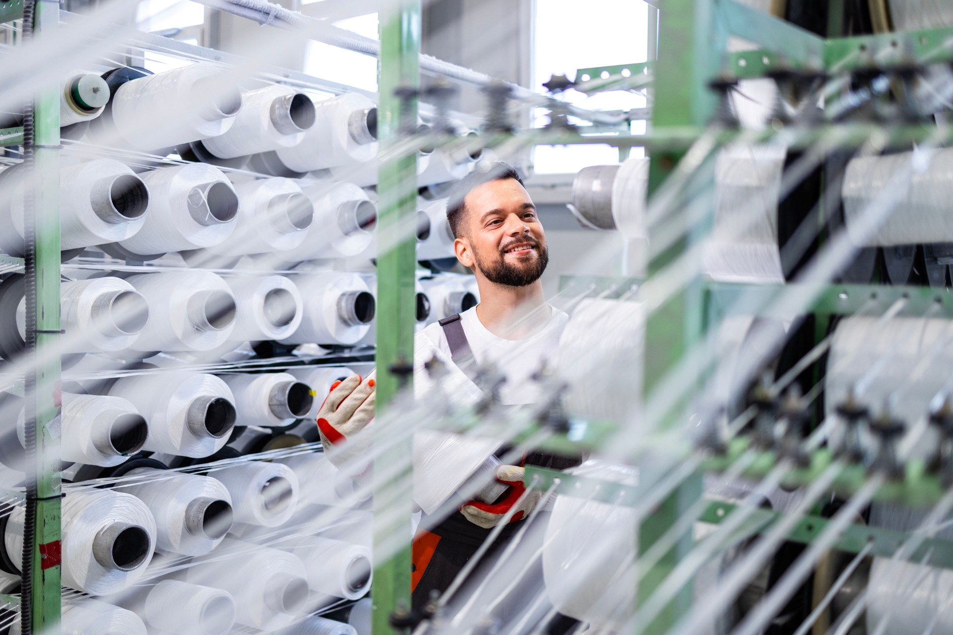 Experienced textile factory worker changing thread spool on industrial knitting machine.